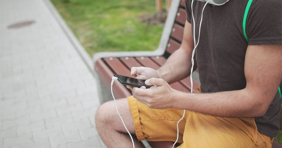 man wearing headphones holding smart phone sitting on a bench