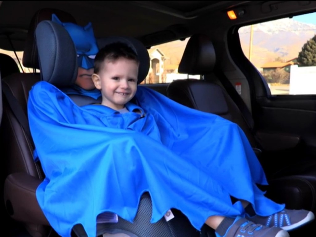 Kid in batman booster seat using cape as blanket