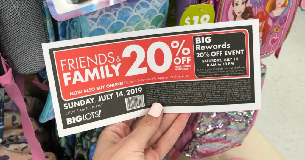 Hand holding big lots friends & family discount coupon in front of school backpacks in store