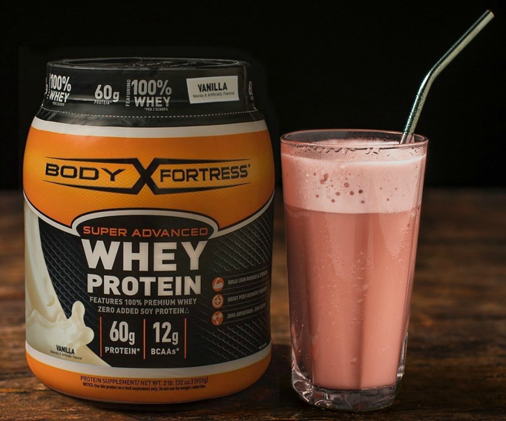 Large canister of Whey protein next to a Protein Shake in a glass with a straw