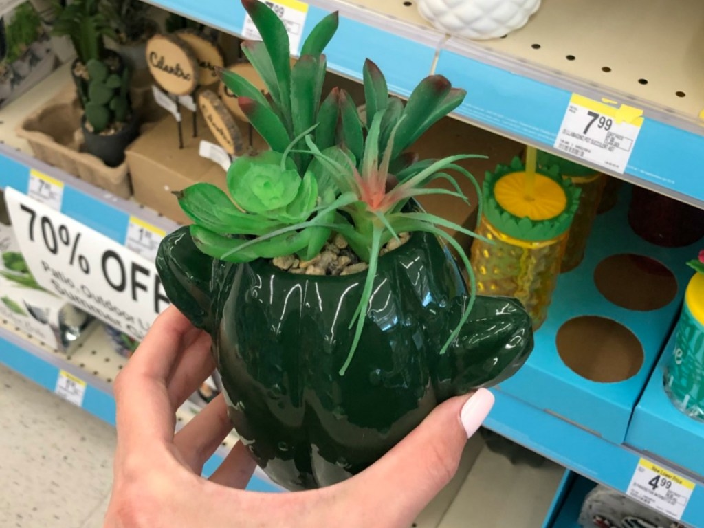 hand holding green pot with plants in it