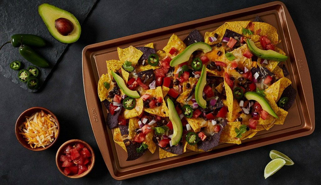 Loaded nachos on a copper baking sheet on a dark surface with toppings