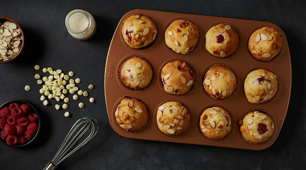 a dozen muffins in a copper colored muffin tin with ingredients
