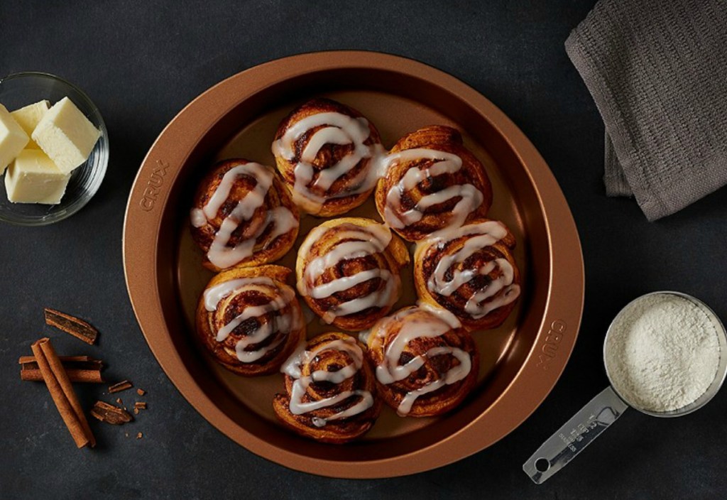 Cinnamon Rolls in copper cake pan on dark surface with ingredients
