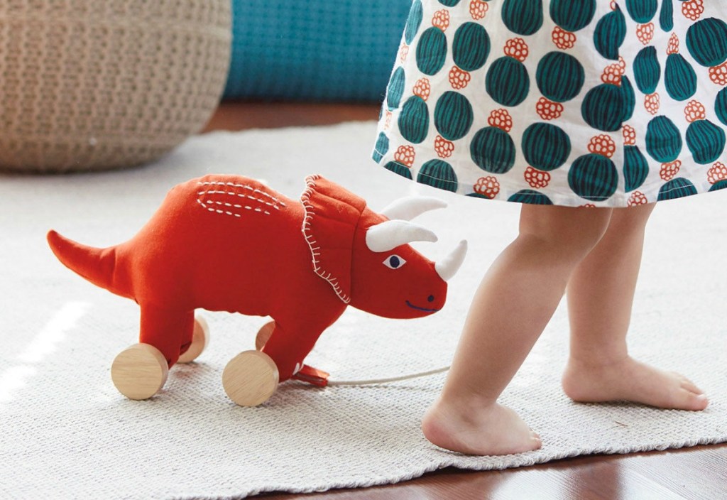 toddler girl walking rhino pull toy through living room