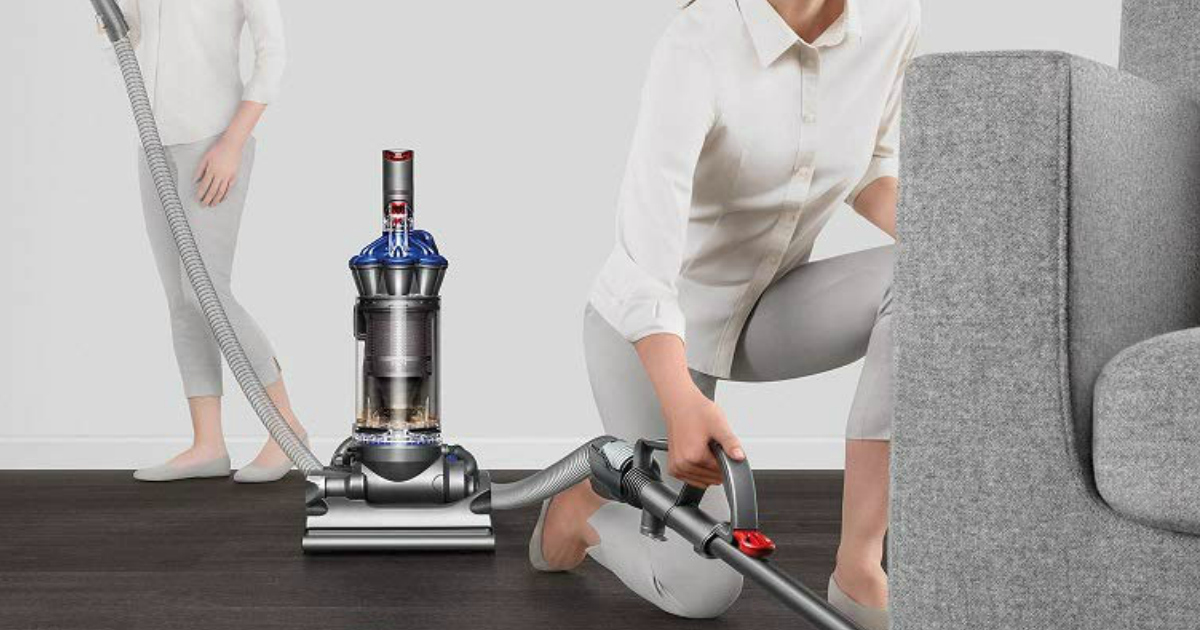 Woman using a Dyson vacuum under a grey armchair