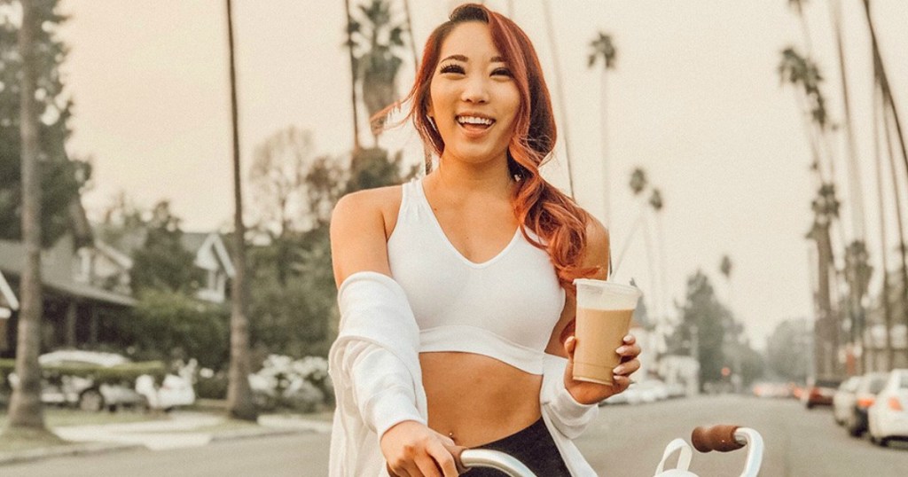 girl riding bike drinking ice coffee wearing a white sports bra