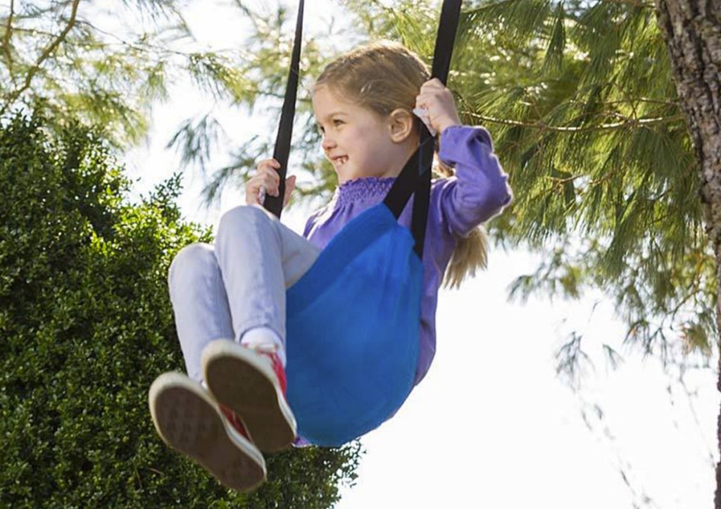 Girl swinging on a blue sling-shaped swing in a tree