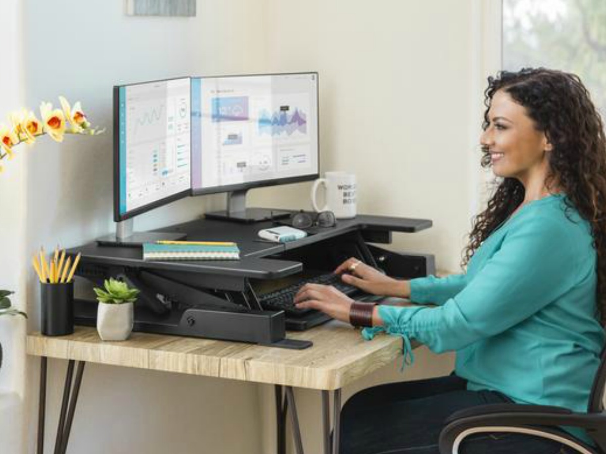 woman sitting at an adjustable height desk looking at computer screens