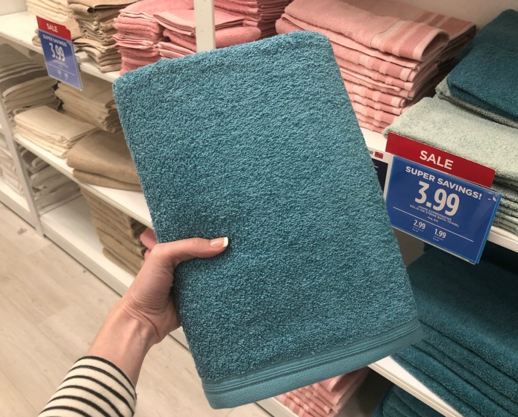 Teal-colored bath towel in-hand in front of store display of towels at JCPenney
