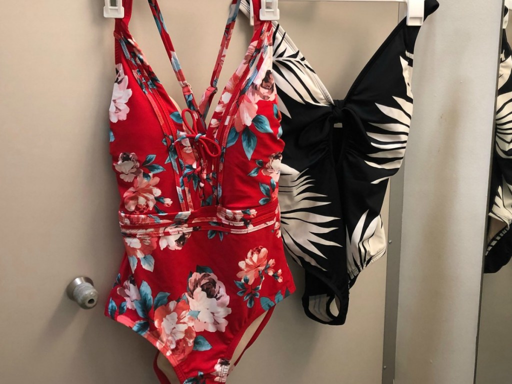 Red floral one-piece swimsuit hanging next to black swimsuit with palm leaves
