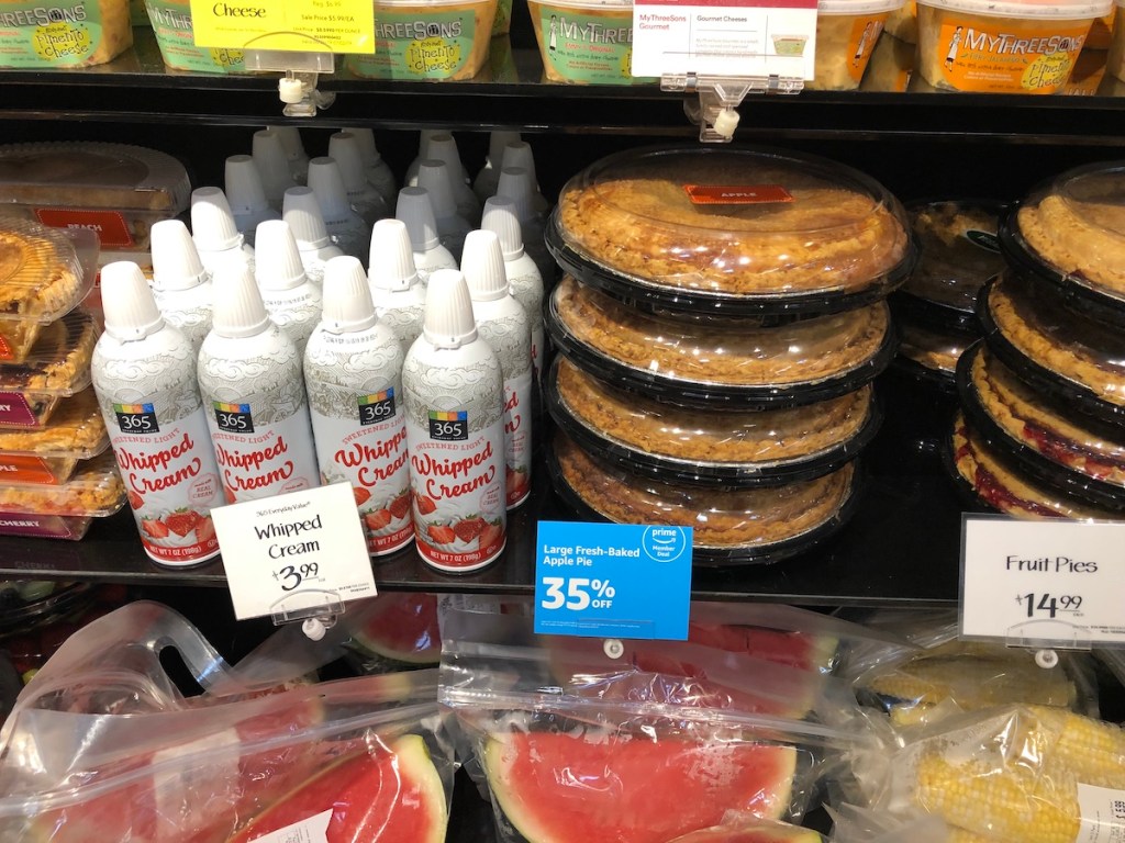 shelf with Large Fresh-Baked Apple Pie, whipped cream, and fruit at whole foods in cooler