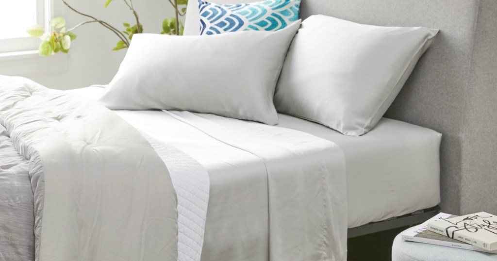 Light beige-colored sheets on a queen size bed with throw pillows and fabric headboard