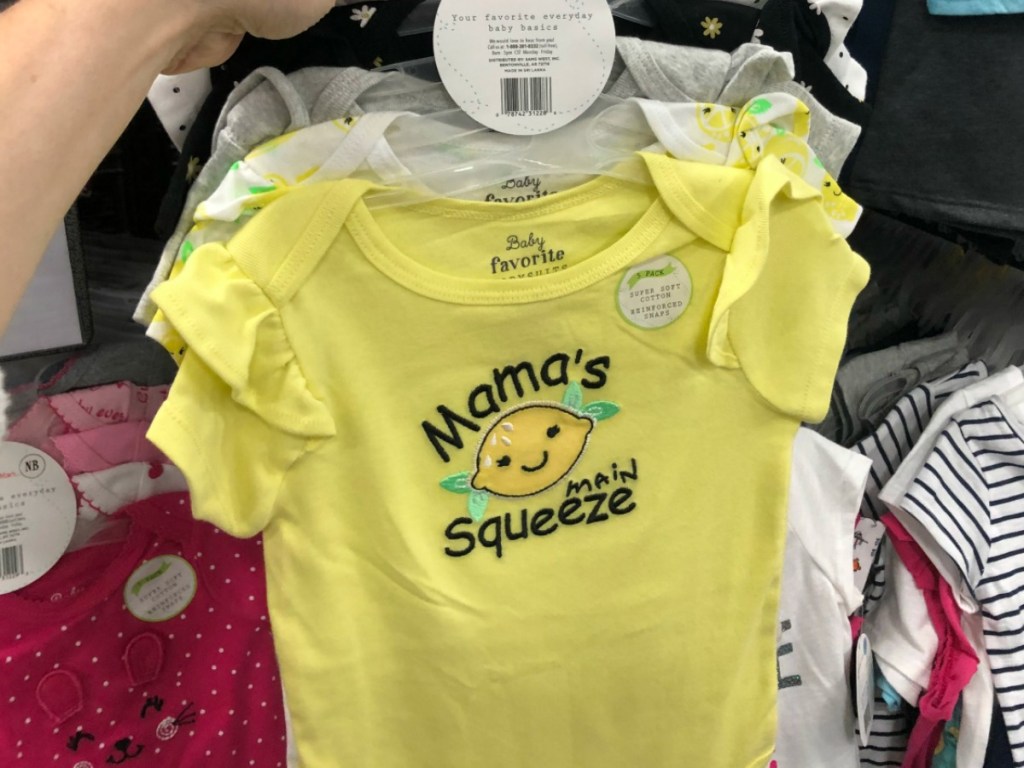 hand holding baby bodysuits on hanger by store display