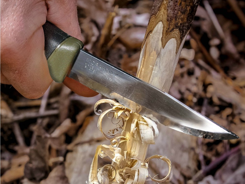 Man holding Morakniv Companion Knife cutting bark