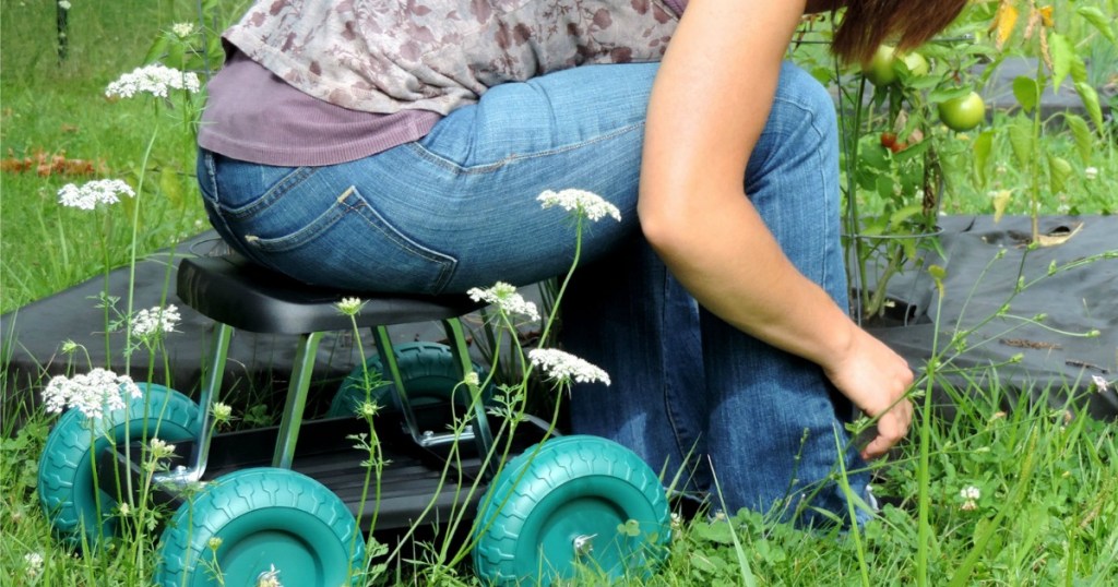 woman seated on a rolling scooter outside doing gardening