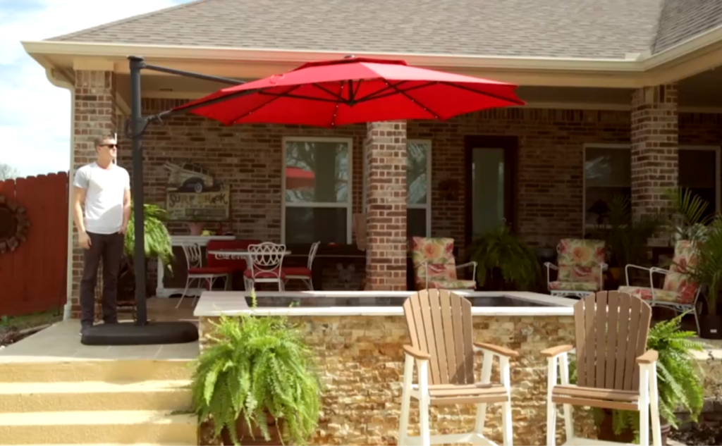 Simply Shade Red Offset Pre-lit 11-ft Auto-tilt Octagon Patio Umbrella with Black Aluminum Frame and Base in backyard over hot tub