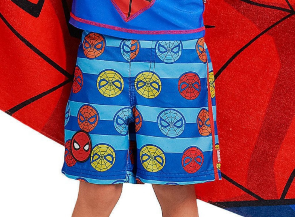 Boy wearing spider-man themed swim trunks while holding a Spider-man towel