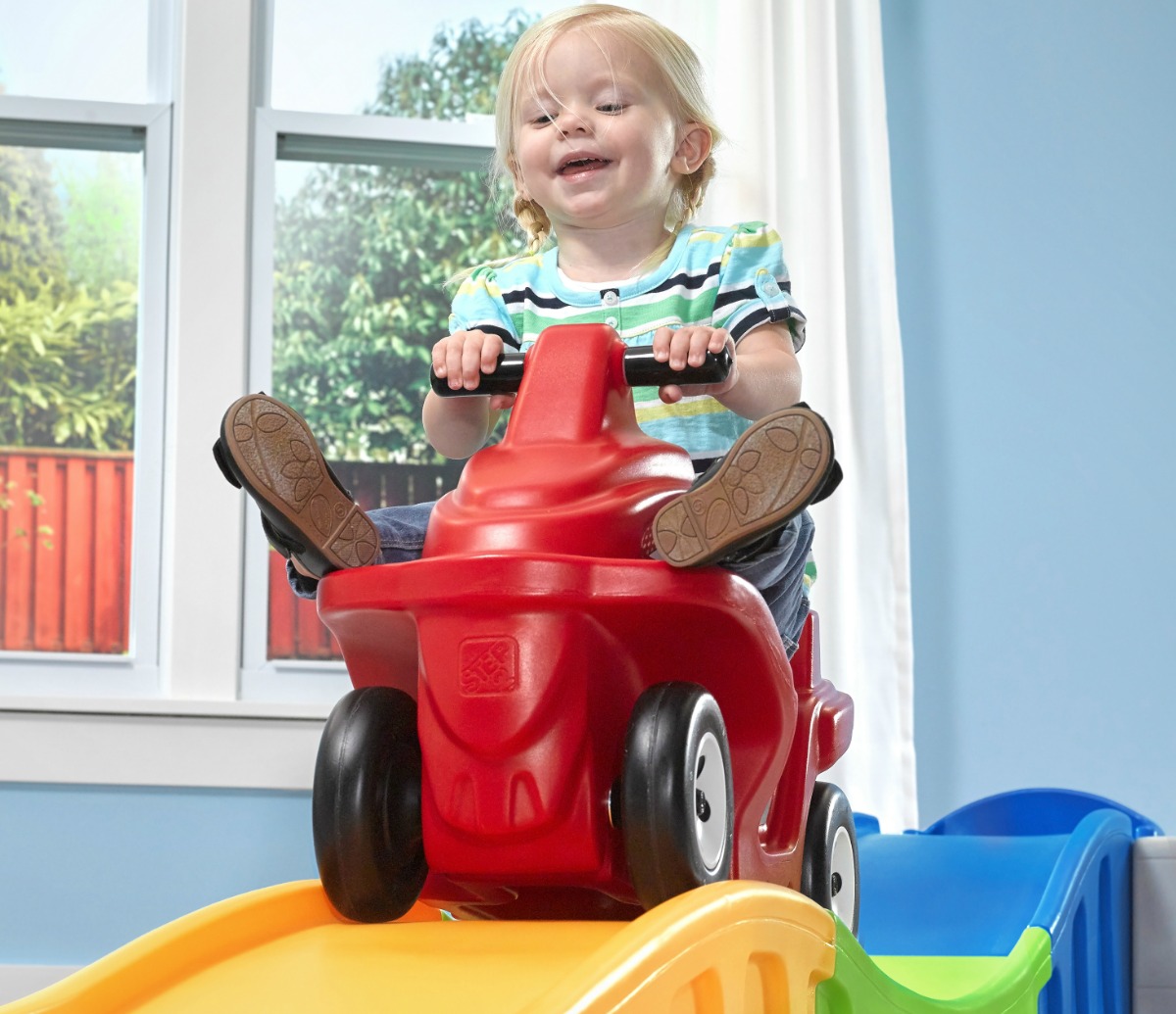 Toddler boy joyfully riding a red roller coast toy