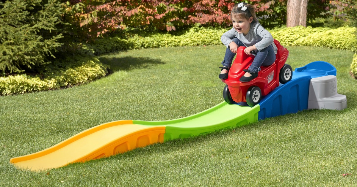 Young girl rides on a roller coast toy in grass filled yard