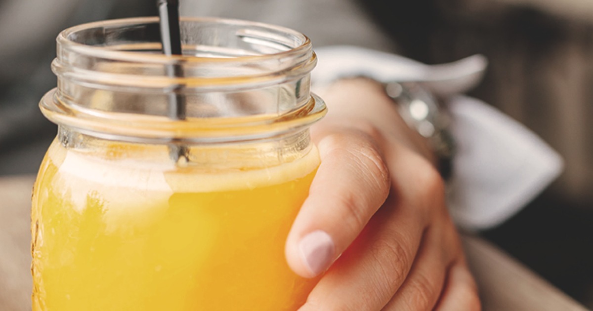 woman holding mason jar filled with orange liquid and a straw