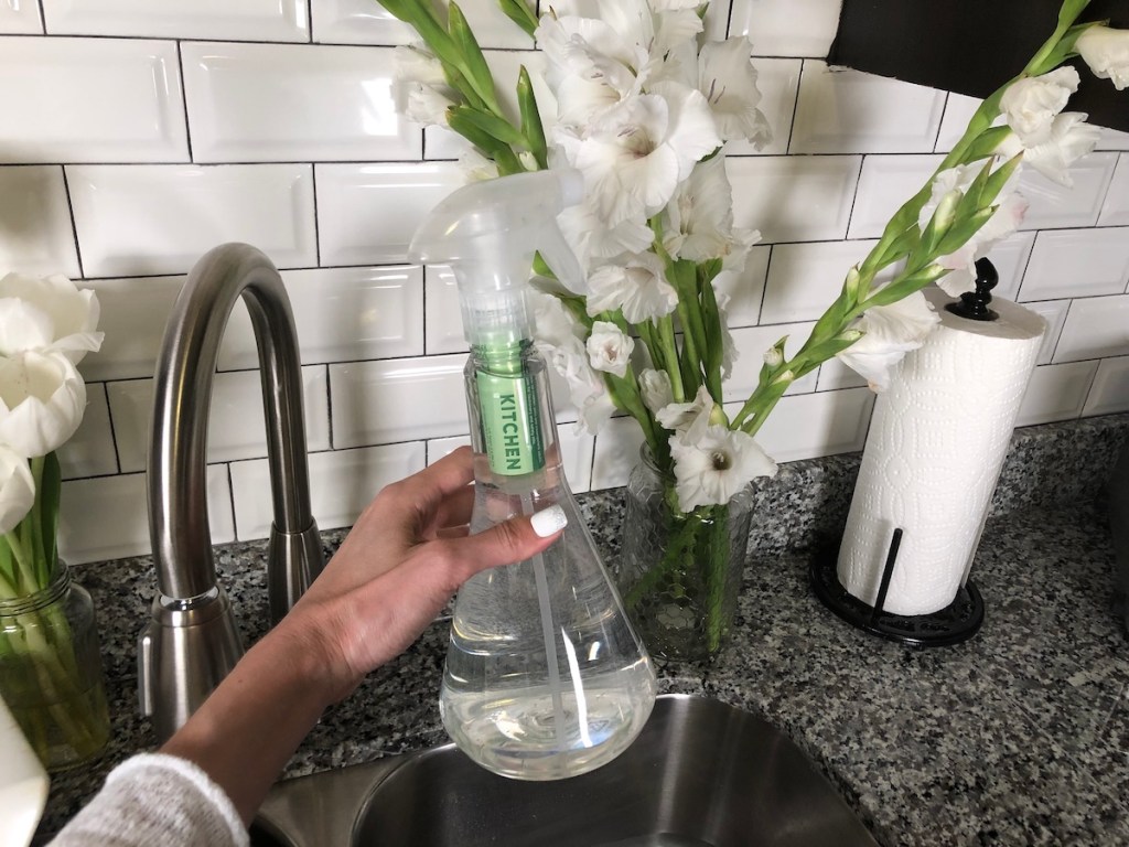 hand holding Truman's kitchen cleaner in kitchen with flowers