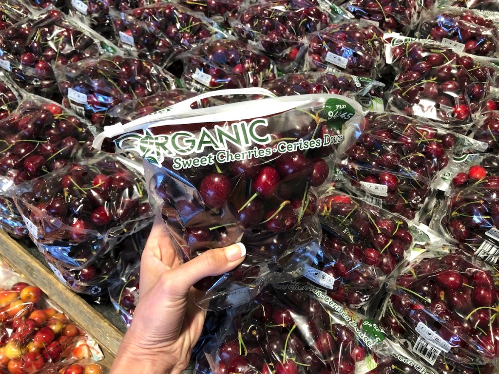 hand holding organic sweet cherries in front of cherries display in whole foods
