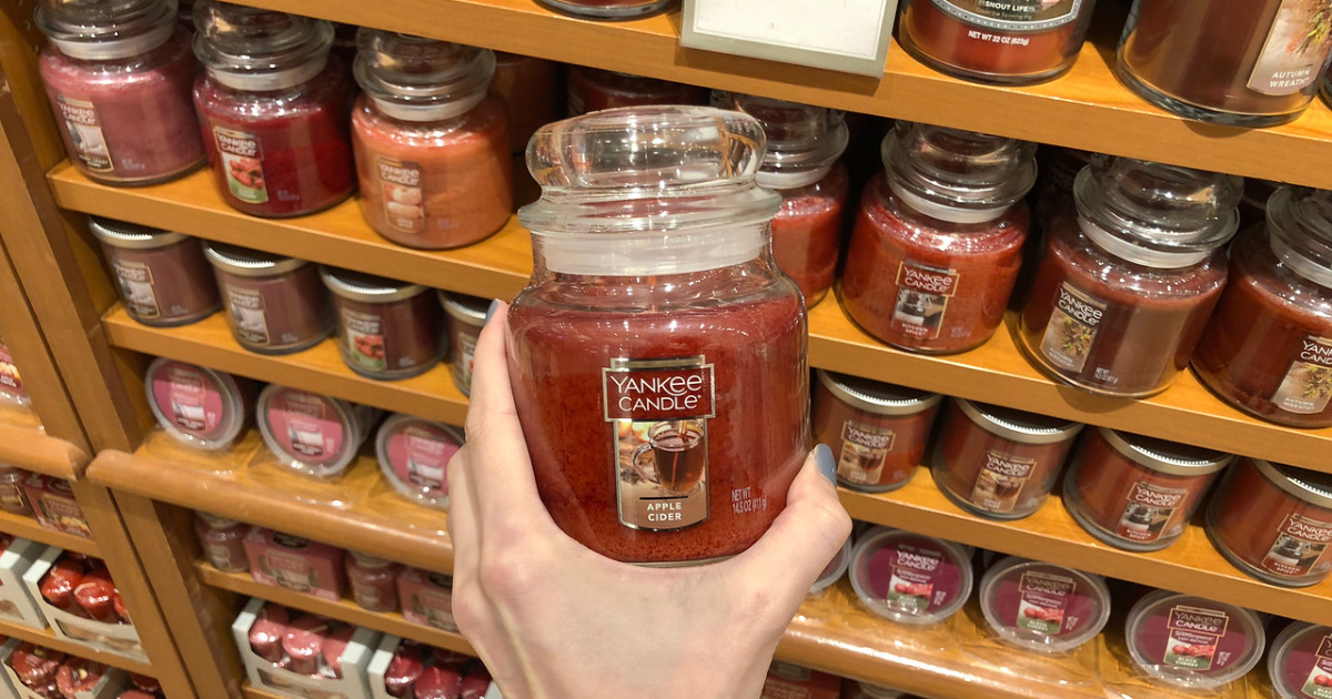 hand holding a medium yankee candles in front of a shelf full of candles