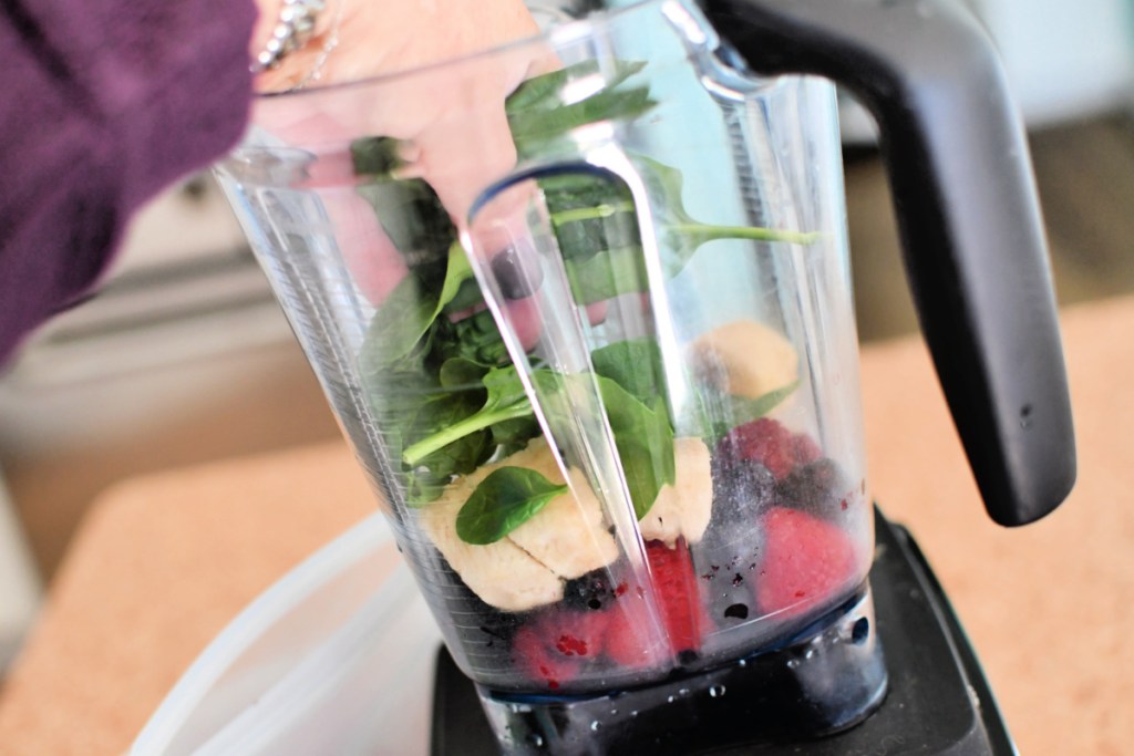 adding spinach to blender with berries