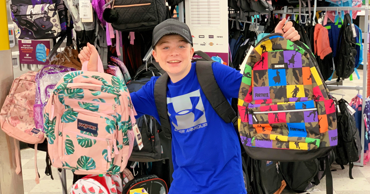 boy in blue under armour shirt holding up backpacks in-store