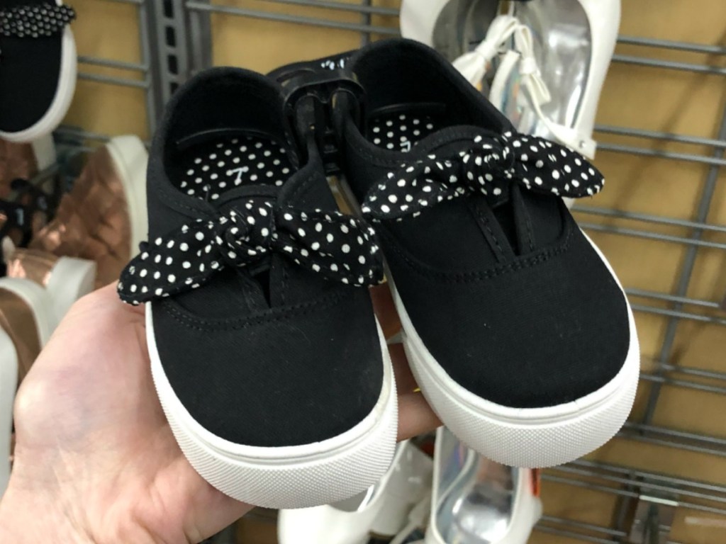 hand holding small black shoes with polka dot ribbons