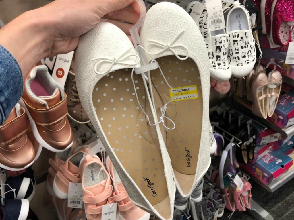 hand holding pair or creme kids shoes by store display