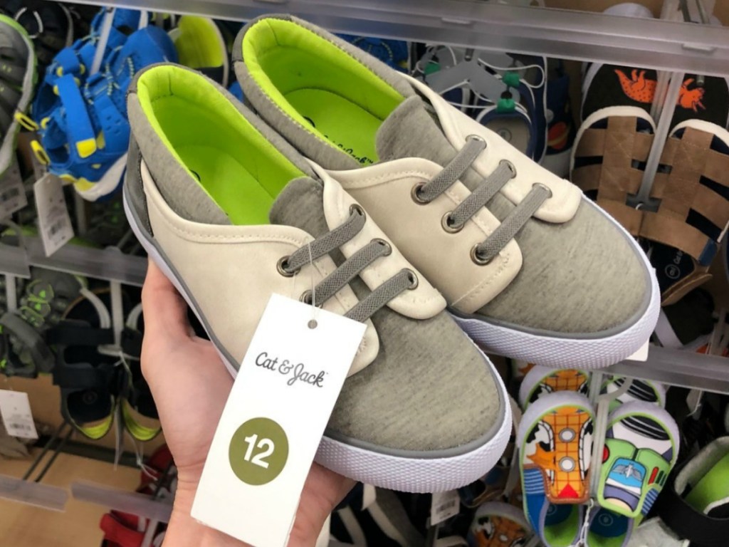 hand holding pair of sneakers in tan and green by store display