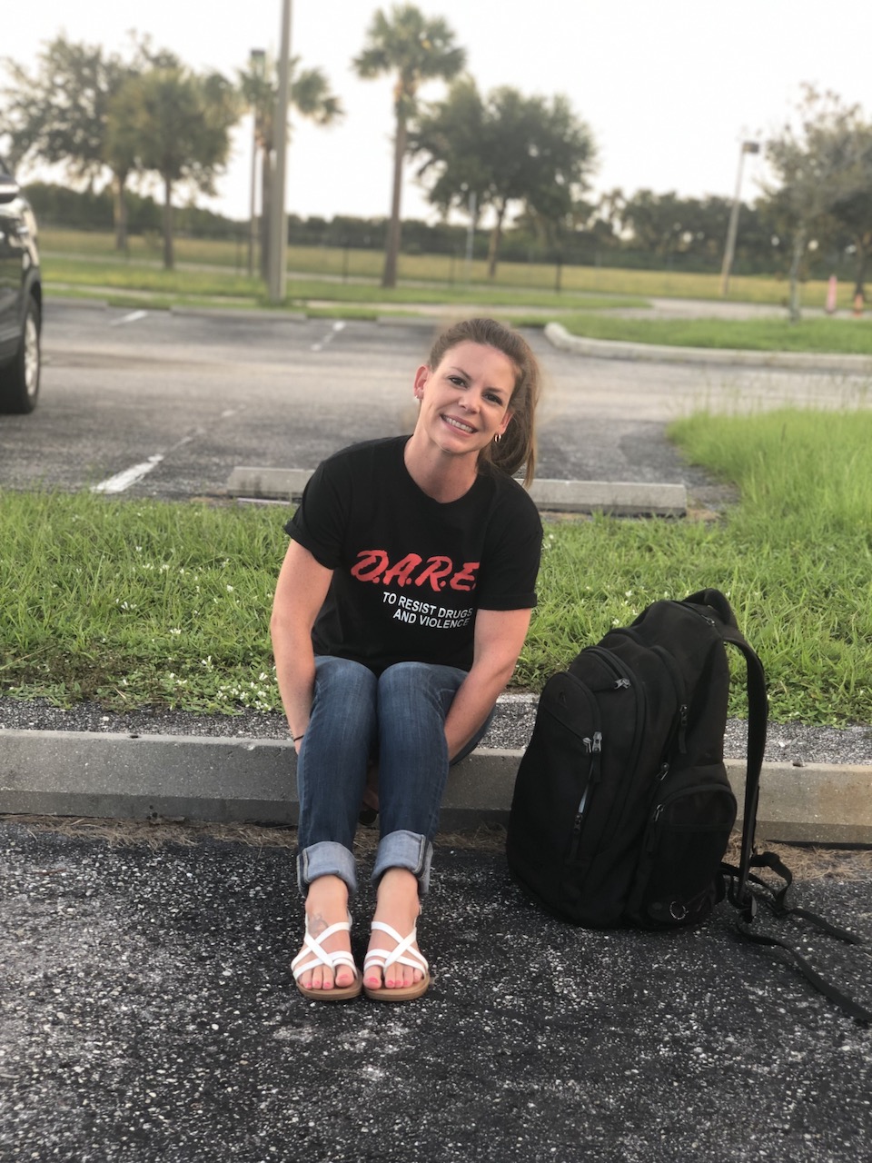 woman wearing DARE shirt in parking lot with black bookbag