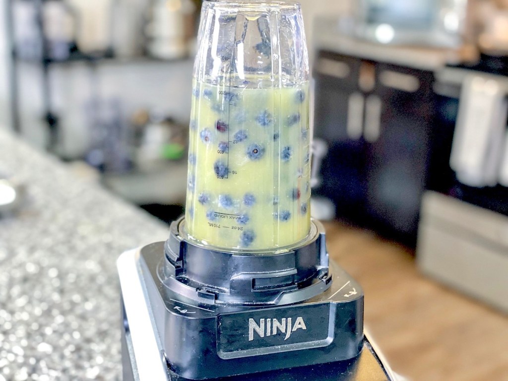 ninja blender on kitchen counter with clear glass full of blueberries and juice