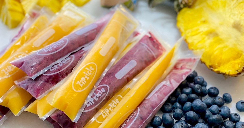 purple and orange frozen popsicles sitting on counter with pineapple and blueberries
