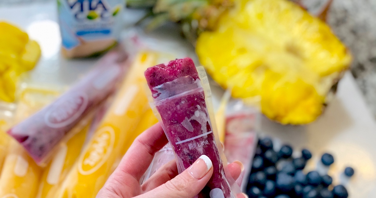 hand holding a purple frozen popsicle with fruit in background