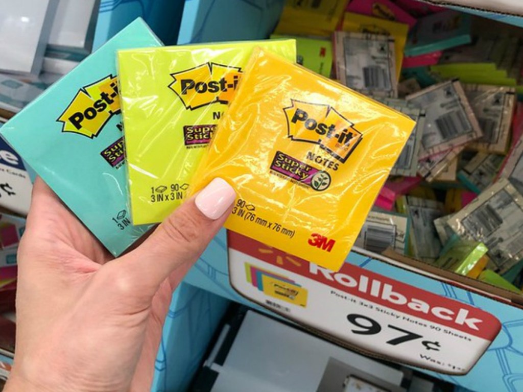 hand holding 3 packages of sticky notes by store display