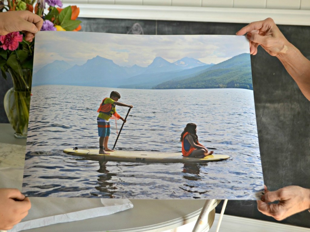 hands holding up a printed poster of kids on a lake