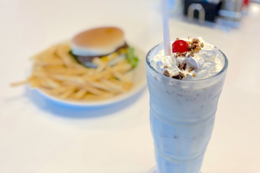 close up of milkshake on counter with plate of cheeseburger and fries