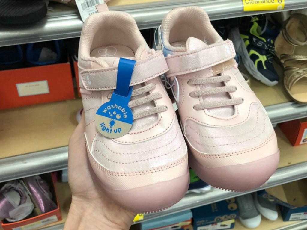 hand holding cute pair of pink sneakers by store display