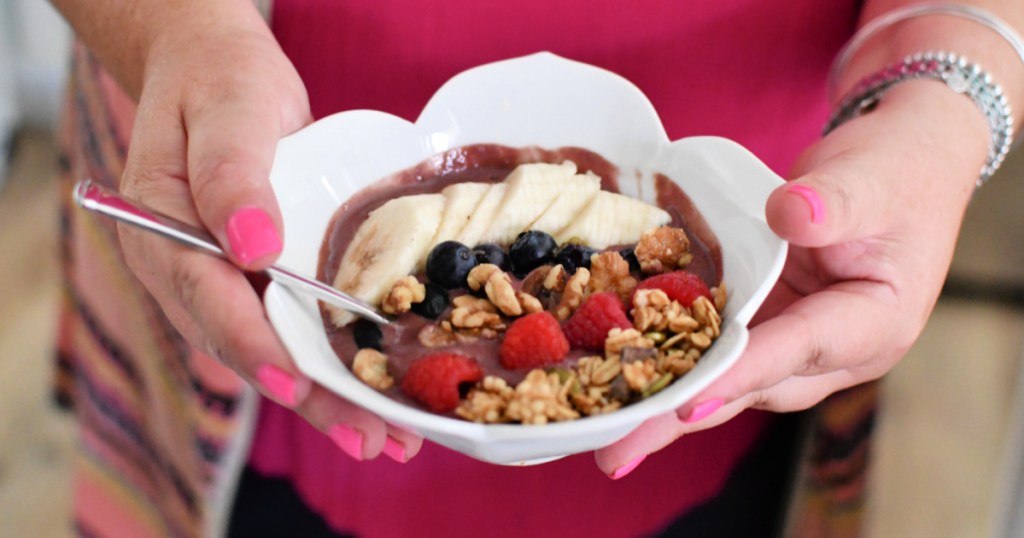 woman holding a acai bowl with fruit and nut toppings