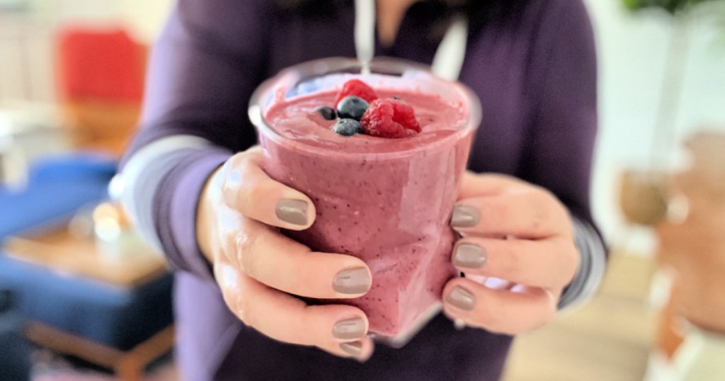woman holding a berry and spinach smoothie