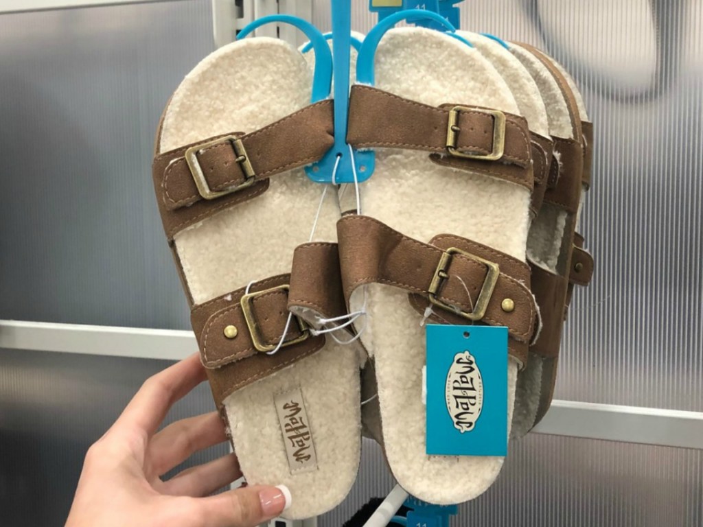 woman holding pair of fuzzy sandals in store by display