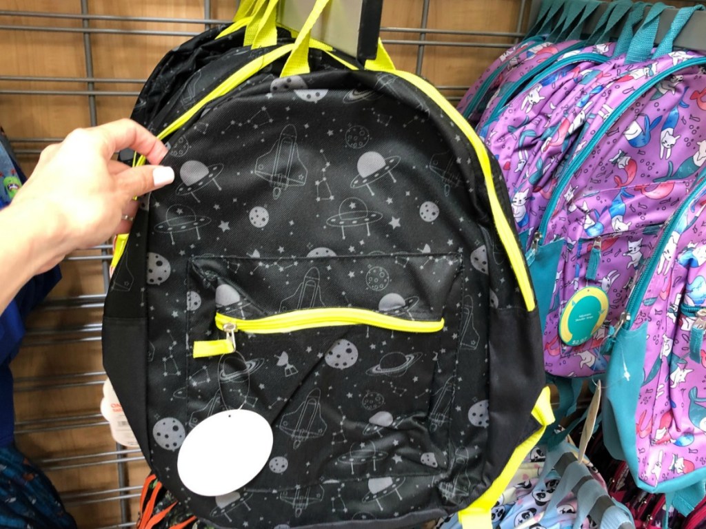 hand holding black kids backpack by store display