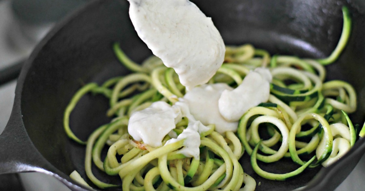 zucchini cut into swirls in fry pan with spoon and white sauce