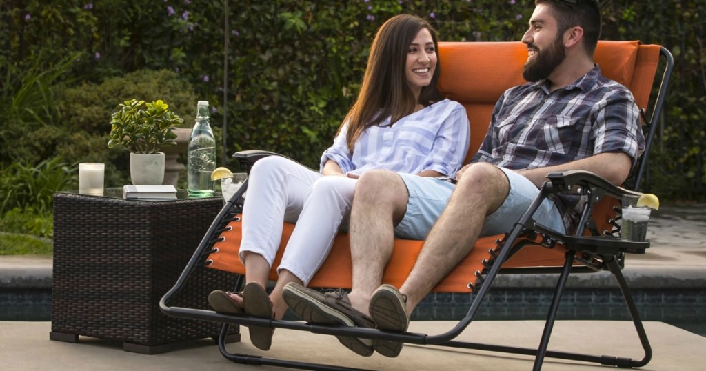 Couple sitting together in a double wide lounger chair on patio with drinks on end table