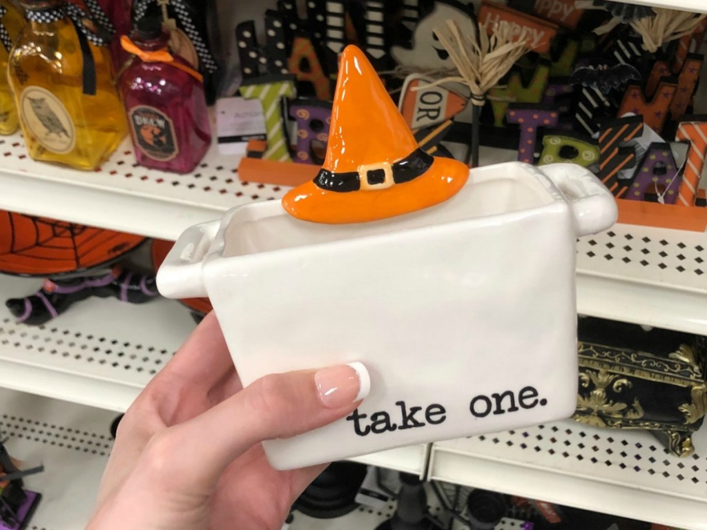 White candy dish that says "take one" and has an orange witches hat in-hand in front of in-store display