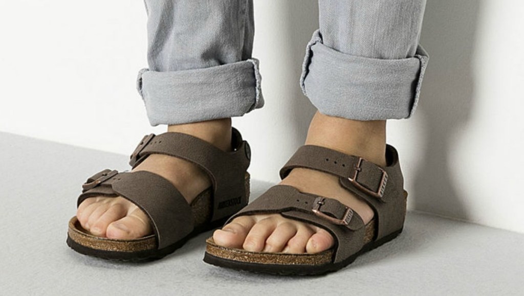 Dark brown kids sandals on kids feet with gray pants