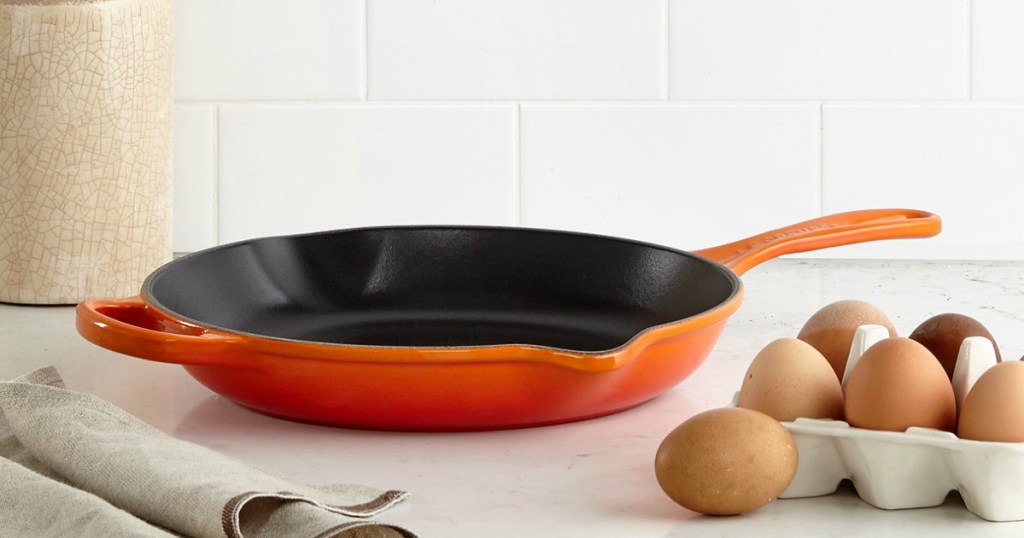 orange Le Crueset frying pan near eggs on a kitchen counter